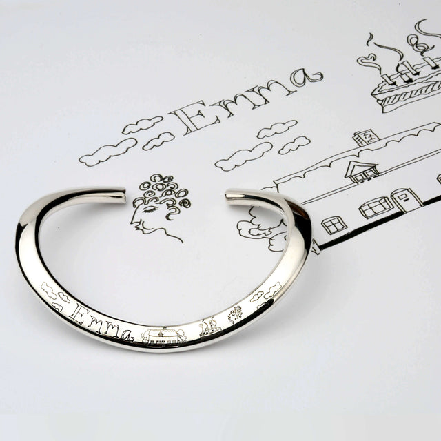 A silver bangle with an engraving of hand designed images and the name Emma.